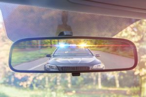 police car with lights on in review mirror | Legal Ramifications of DUI 